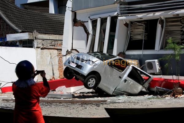 Warga menyaksikan sebuah mobil yang tertimpa bangunan akibat gempa di Padang, Sumatera Barat, Jumat (210). Gempa bumi berskala 7,6 skala richter yang mengguncang Padang mengakibatkan sedikitnya 500 orang meninggal dan ribuan bangunan